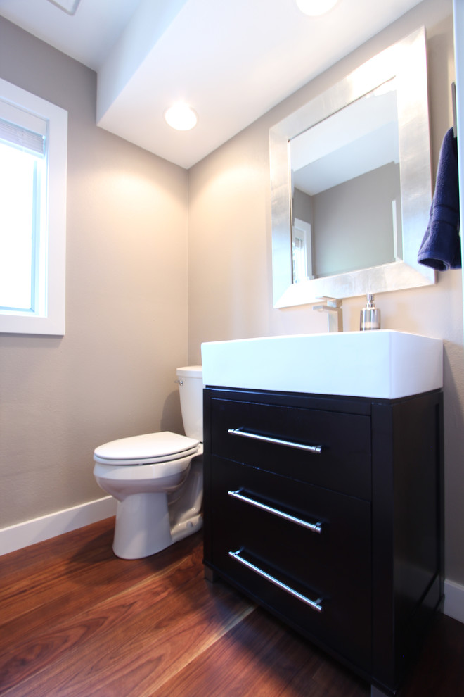 This is an example of a small modern cloakroom in Other with freestanding cabinets, dark wood cabinets, a two-piece toilet, grey walls, medium hardwood flooring, an integrated sink, solid surface worktops and brown floors.