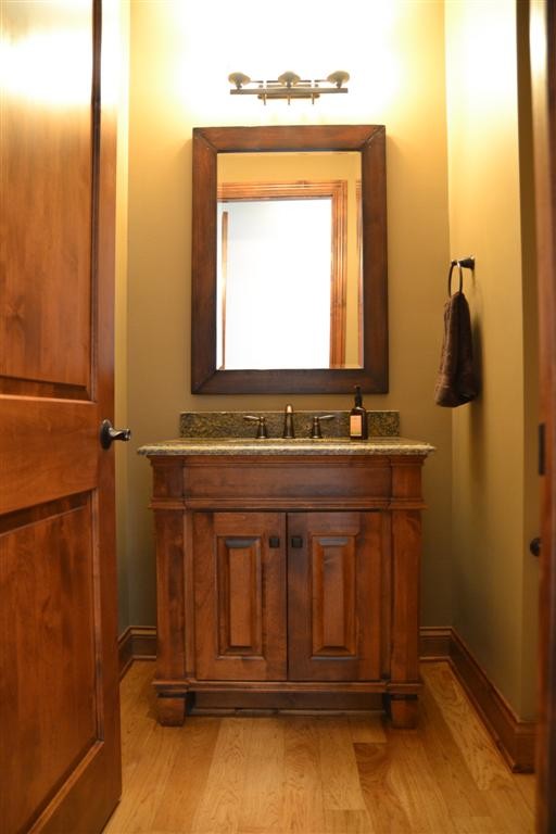 Small elegant light wood floor and beige floor powder room photo in Milwaukee with furniture-like cabinets, medium tone wood cabinets, beige walls, an undermount sink and granite countertops