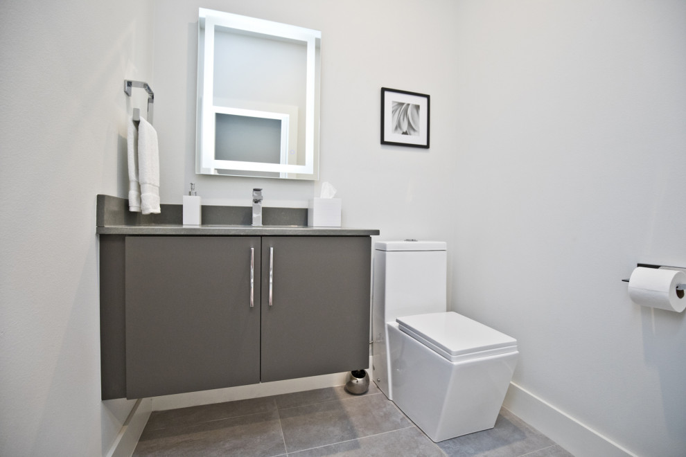 Moderne Gästetoilette mit flächenbündigen Schrankfronten, grauen Schränken, Toilette mit Aufsatzspülkasten, weißer Wandfarbe, Unterbauwaschbecken, grauem Boden und grauer Waschtischplatte in Sonstige