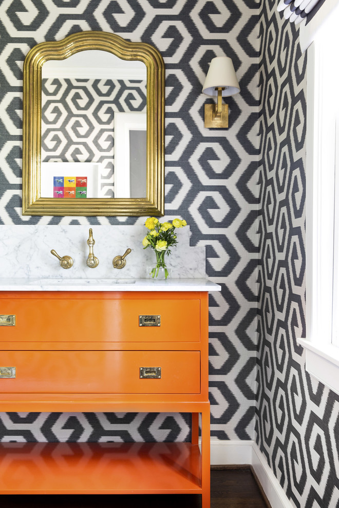 Klassisk inredning av ett vit vitt toalett, med möbel-liknande, orange skåp, flerfärgade väggar, mörkt trägolv, ett undermonterad handfat och brunt golv