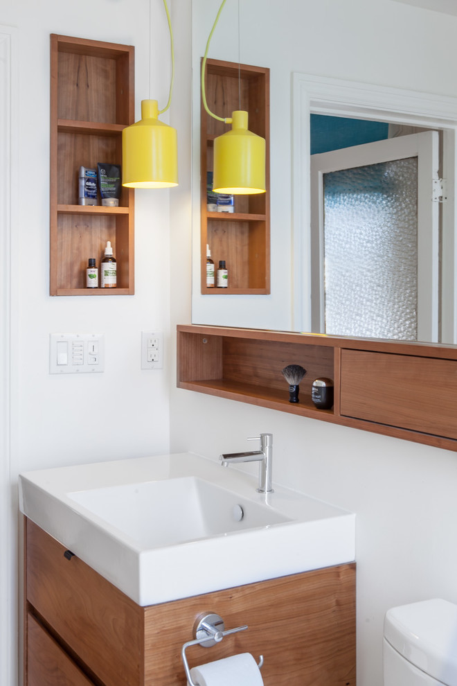 Idee per un bagno di servizio minimal con ante lisce, ante in legno scuro, pareti bianche e lavabo integrato