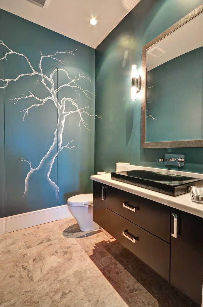 Mid-sized trendy limestone floor powder room photo in Miami with flat-panel cabinets, dark wood cabinets, a one-piece toilet, blue walls, a vessel sink and solid surface countertops