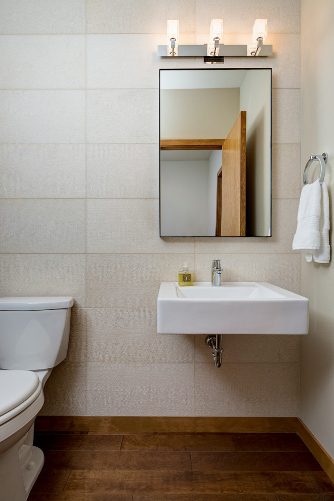 Idée de décoration pour un WC et toilettes minimaliste de taille moyenne avec WC séparés, un carrelage beige, des carreaux de céramique, un mur beige, parquet foncé et un lavabo suspendu.