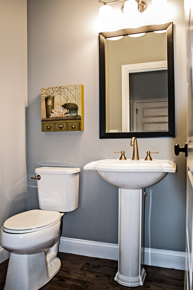 Bild på ett mellanstort amerikanskt toalett, med en toalettstol med separat cisternkåpa, grå väggar, mellanmörkt trägolv, ett piedestal handfat och brunt golv