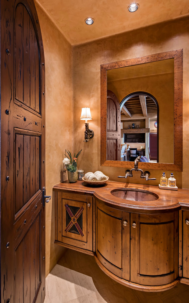 На фото: туалет в стиле фьюжн с фасадами островного типа, унитазом-моноблоком, полом из известняка, врезной раковиной и столешницей из дерева