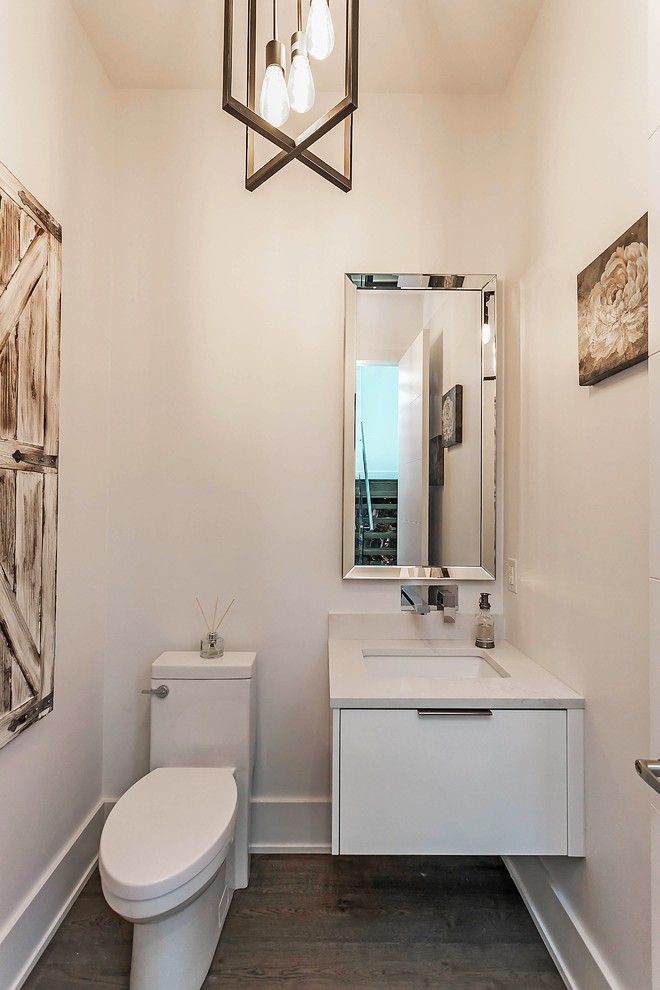 Aménagement d'un WC et toilettes classique avec un placard à porte plane, des portes de placard blanches, WC à poser, un mur blanc, un sol en bois brun, un lavabo encastré et un plan de toilette en quartz modifié.