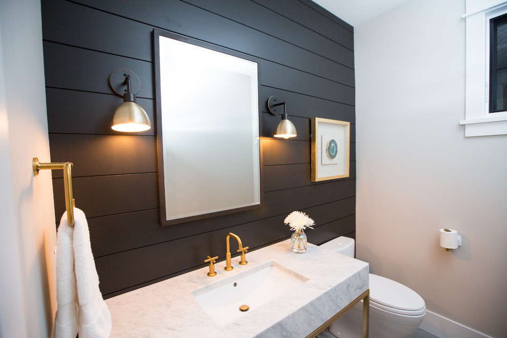 Modern inredning av ett mellanstort vit vitt toalett, med möbel-liknande, vita skåp, en toalettstol med separat cisternkåpa, svarta väggar, klinkergolv i porslin, ett undermonterad handfat, marmorbänkskiva och grått golv