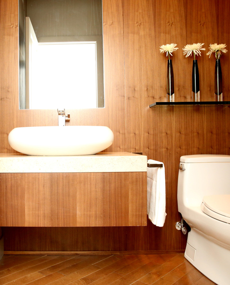 Moderne Gästetoilette mit Aufsatzwaschbecken, flächenbündigen Schrankfronten, hellbraunen Holzschränken, Kalkstein-Waschbecken/Waschtisch, Toilette mit Aufsatzspülkasten, beigen Fliesen, beiger Wandfarbe und braunem Holzboden in Calgary