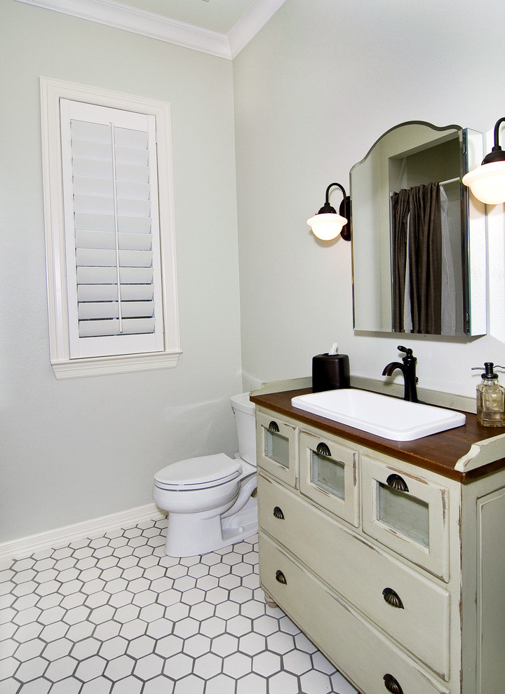 Inspiration for a timeless white tile porcelain tile powder room remodel in Dallas with a drop-in sink, furniture-like cabinets, wood countertops, a two-piece toilet, gray walls and distressed cabinets