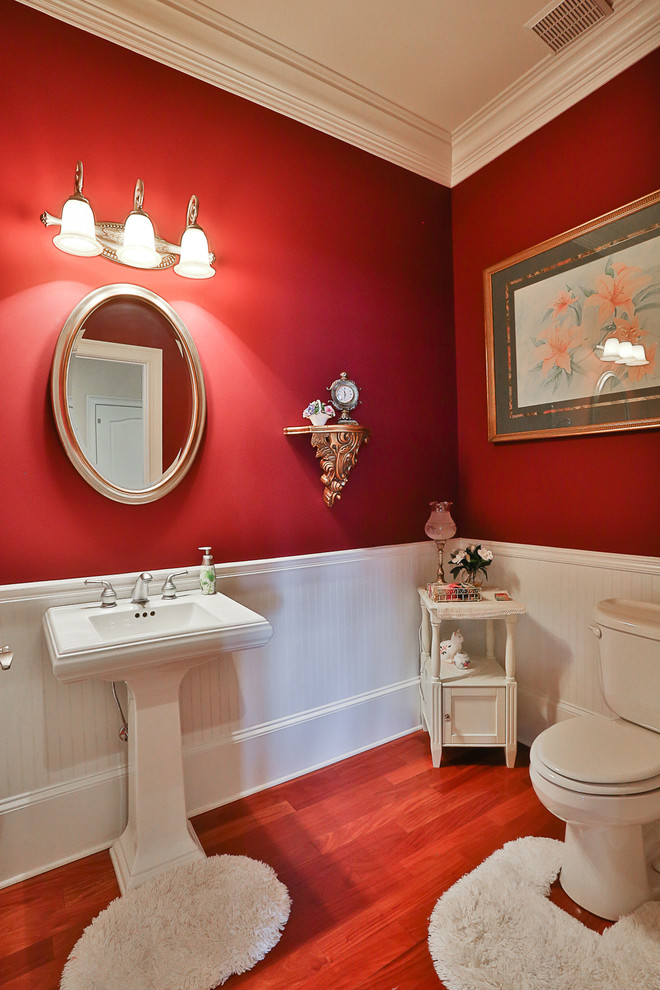 アトランタにあるお手頃価格の広いトラディショナルスタイルのおしゃれなトイレ・洗面所 (ペデスタルシンク、分離型トイレ、赤い壁、無垢フローリング、茶色い床) の写真