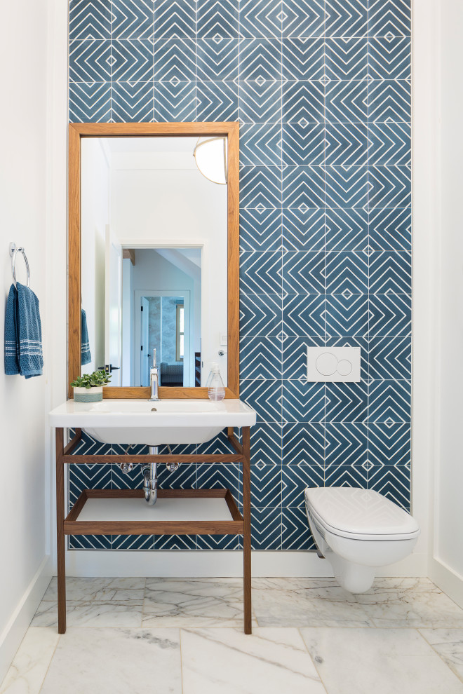 Bild på ett funkis toalett, med en vägghängd toalettstol, blå kakel, vita väggar, ett konsol handfat och vitt golv