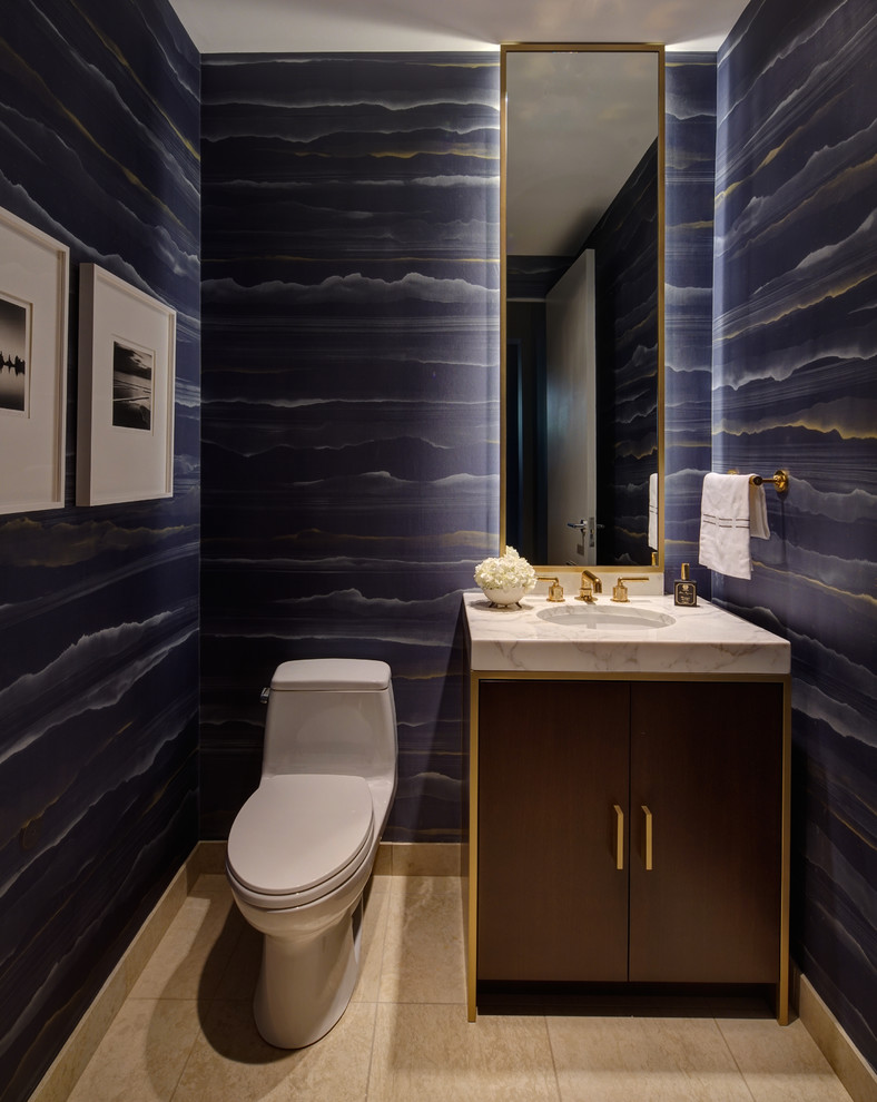 Idée de décoration pour un petit WC et toilettes design en bois foncé avec un placard à porte plane, WC à poser, un carrelage beige, un mur bleu, un sol en calcaire, un lavabo encastré, un plan de toilette en marbre et un sol beige.