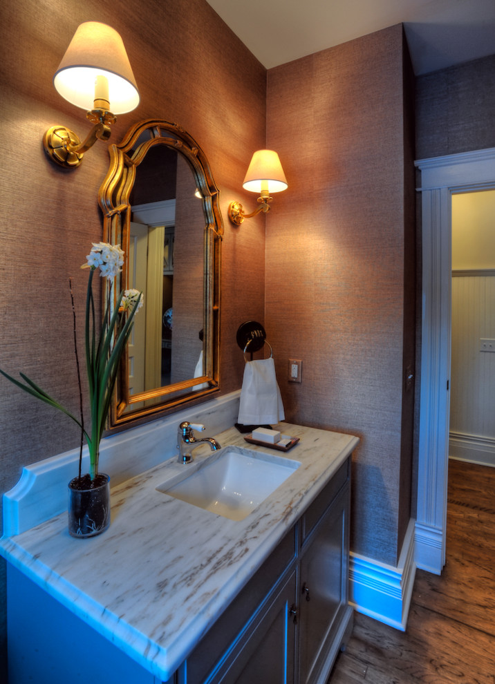 Aménagement d'un WC et toilettes classique avec un mur marron, un sol en bois brun, un lavabo encastré et un plan de toilette en marbre.