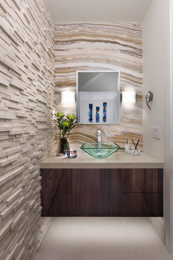 Powder room - small contemporary beige tile gray floor powder room idea in Los Angeles with flat-panel cabinets, dark wood cabinets, a vessel sink, beige countertops and beige walls