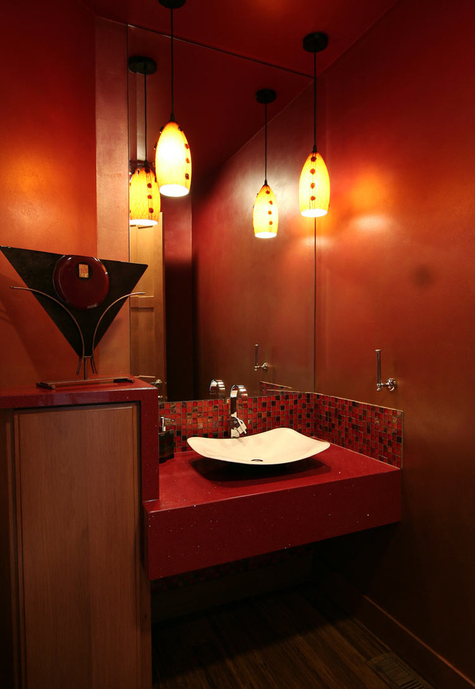Mittelgroße Moderne Gästetoilette mit hellbraunen Holzschränken, roten Fliesen, roter Wandfarbe, dunklem Holzboden, Aufsatzwaschbecken, Mineralwerkstoff-Waschtisch und roter Waschtischplatte in Seattle