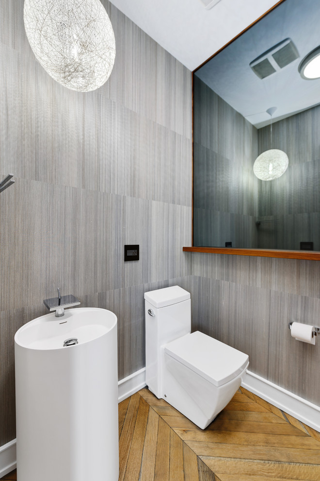 Esempio di un bagno di servizio design con WC monopezzo, piastrelle grigie, pavimento in legno massello medio, lavabo a colonna e pavimento marrone