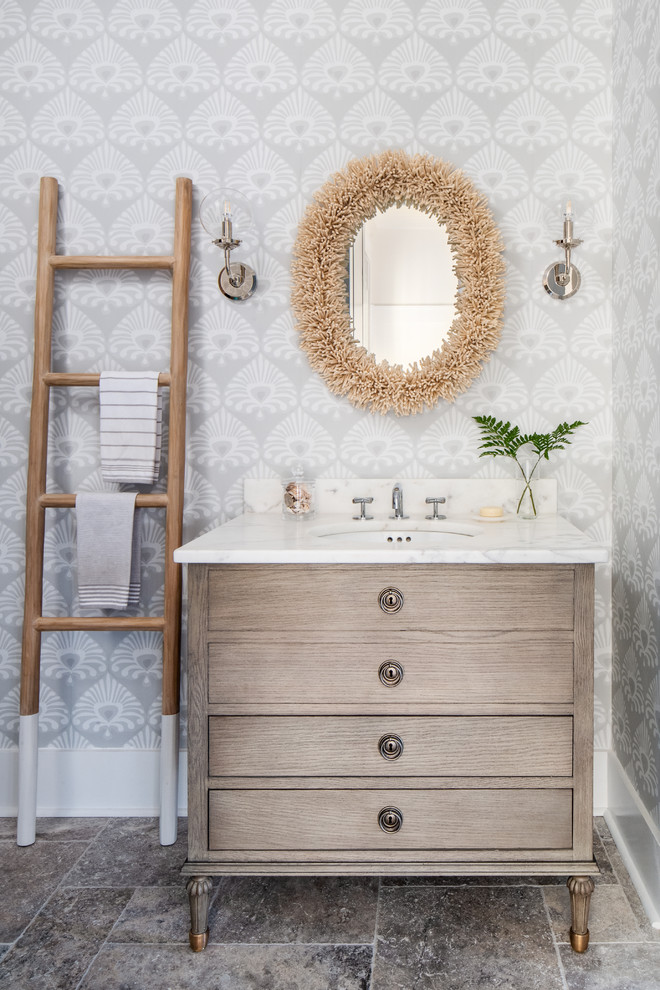 Cette photo montre un WC et toilettes bord de mer en bois clair de taille moyenne avec un placard à porte plane, WC séparés, un mur gris, un sol en travertin, un lavabo encastré, un plan de toilette en marbre, un sol gris et un plan de toilette blanc.