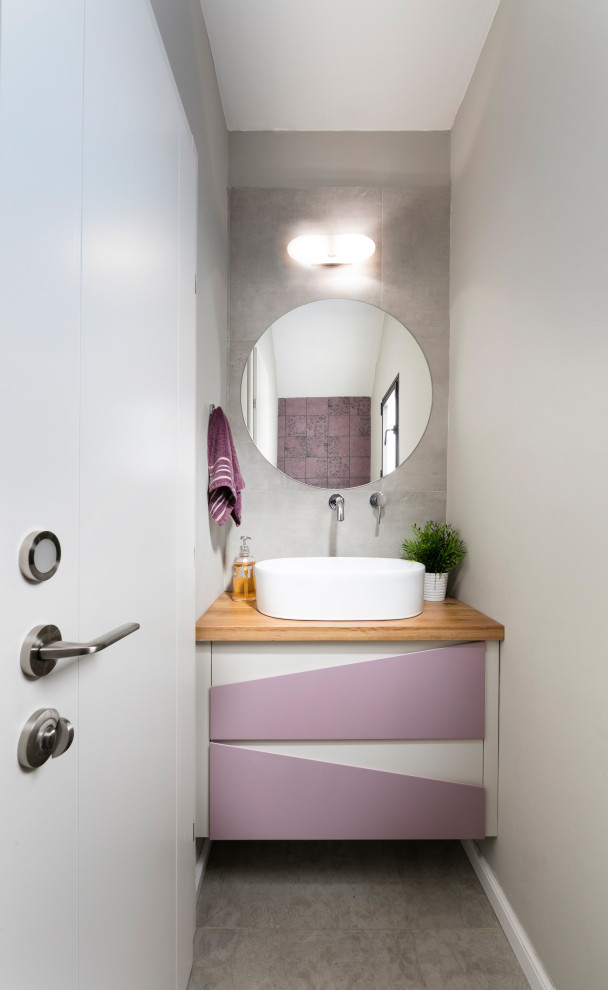 Inspiration för små moderna beige toaletter, med släta luckor, lila skåp, grå kakel, porslinskakel, grå väggar, klinkergolv i porslin, ett fristående handfat, träbänkskiva och grått golv