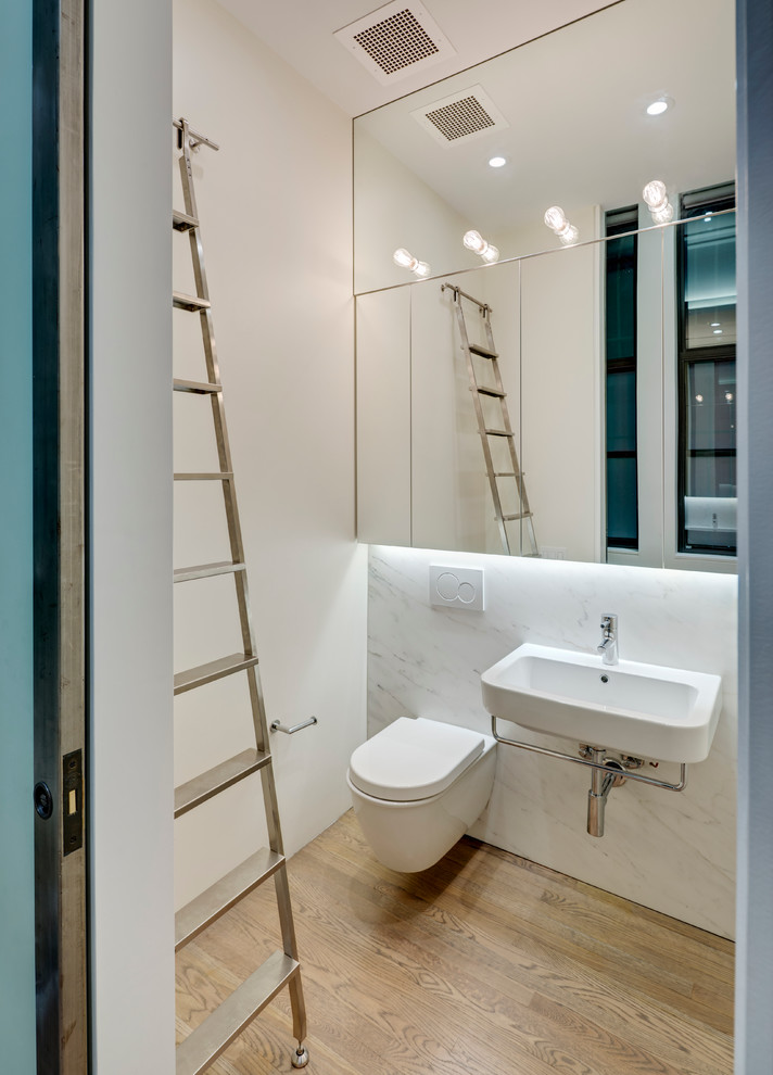 Small minimalist white tile medium tone wood floor powder room photo in New York with a wall-mount toilet, white walls and a wall-mount sink