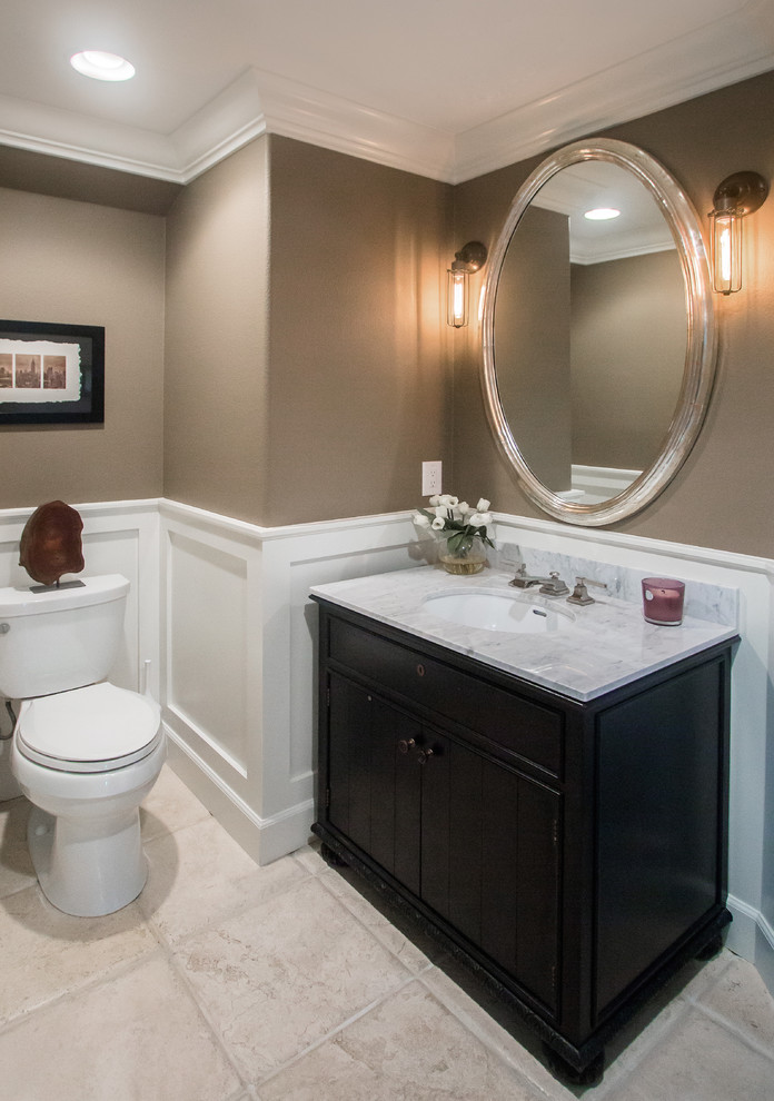 Design ideas for a medium sized traditional cloakroom in Orange County with shaker cabinets, black cabinets, a two-piece toilet, travertine flooring, a submerged sink, marble worktops, beige walls and white worktops.