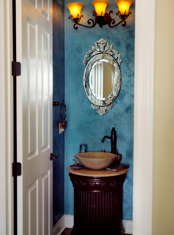 Foto på ett mellanstort eklektiskt toalett, med möbel-liknande, skåp i mörkt trä, blå väggar, ett fristående handfat, en toalettstol med hel cisternkåpa, mellanmörkt trägolv och bänkskiva i travertin