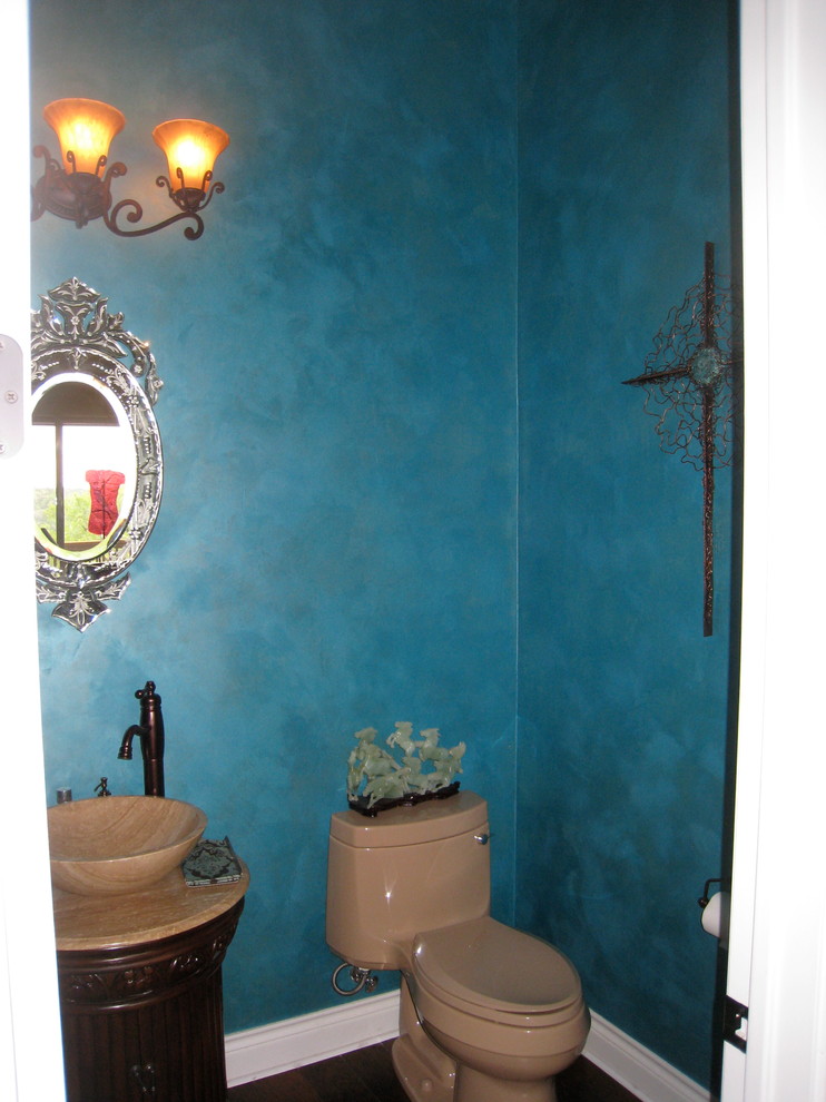 Mittelgroße Eklektische Gästetoilette mit verzierten Schränken, dunklen Holzschränken, blauer Wandfarbe, Aufsatzwaschbecken, Toilette mit Aufsatzspülkasten, braunem Holzboden und Travertin-Waschtisch in Austin