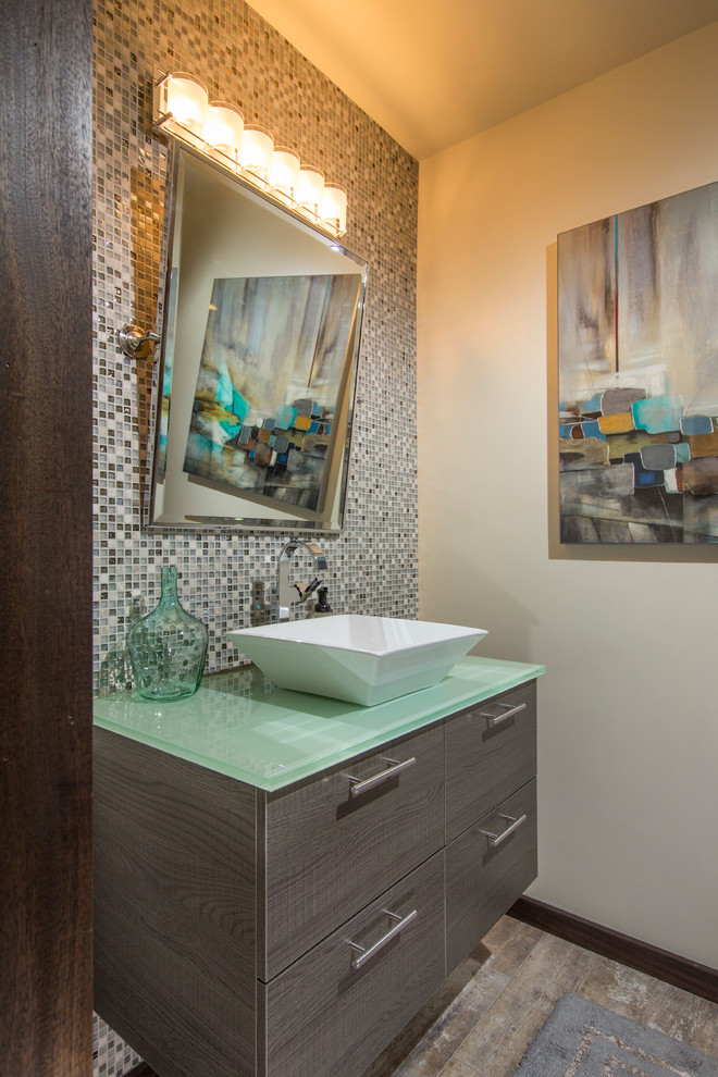 Idéer för funkis grönt toaletter, med ett fristående handfat, släta luckor, grå skåp, bänkskiva i glas, flerfärgad kakel, mosaik, beige väggar och mellanmörkt trägolv