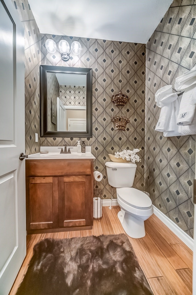 Design ideas for a small contemporary cloakroom in St Louis with shaker cabinets, medium wood cabinets, a one-piece toilet, medium hardwood flooring, a wall-mounted sink, marble worktops, white worktops, a freestanding vanity unit and wallpapered walls.