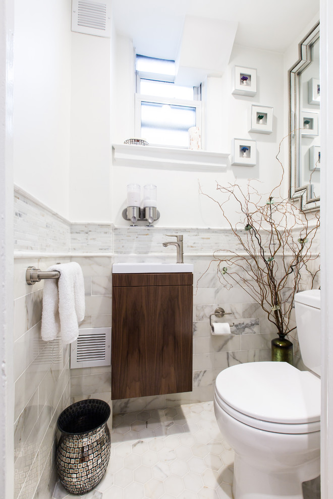 Photo of a small contemporary cloakroom in New York with raised-panel cabinets, dark wood cabinets, a two-piece toilet, white tiles, marble tiles, white walls, marble flooring, a wall-mounted sink and white floors.