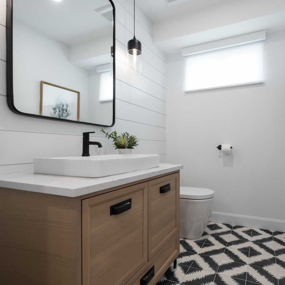 Bild på ett lantligt toalett, med möbel-liknande, skåp i ljust trä, vita väggar, cementgolv, ett fristående handfat, bänkskiva i kvartsit och svart golv