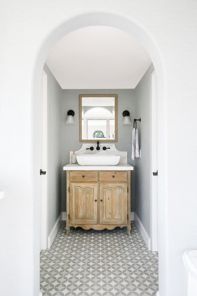 Inredning av ett lantligt toalett, med grå kakel, grå väggar, cementgolv, marmorbänkskiva och flerfärgat golv