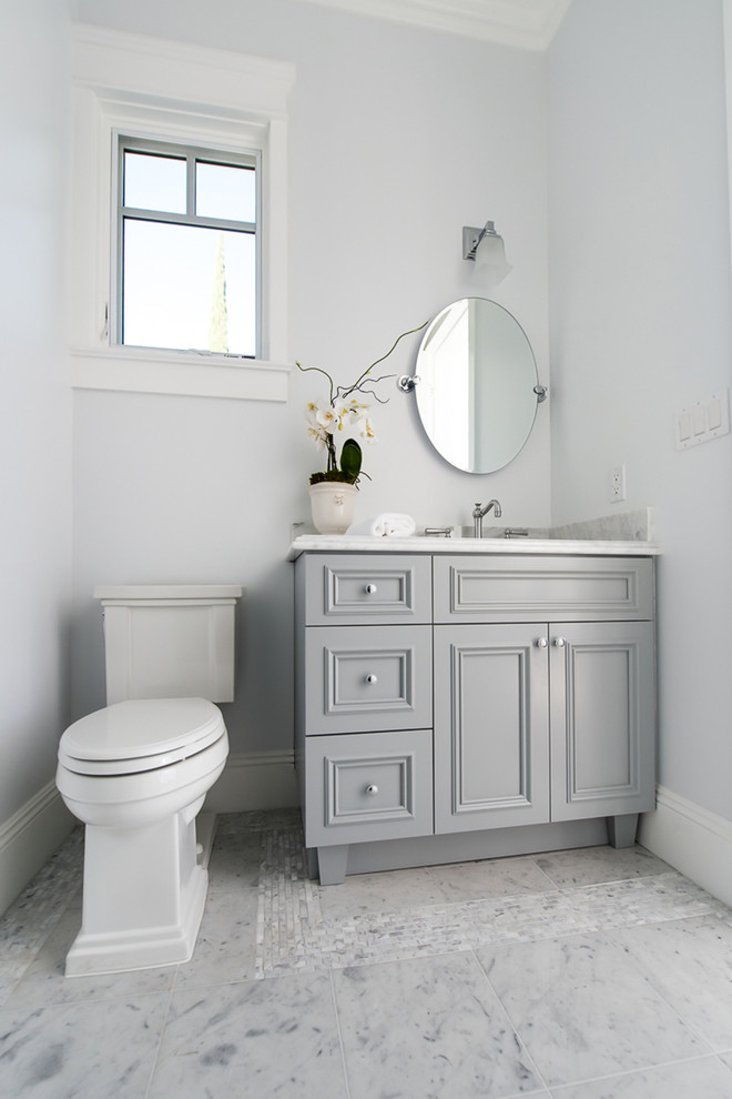 Exemple d'un grand WC et toilettes bord de mer avec des portes de placard grises, un carrelage gris, un mur gris, un sol en marbre, un lavabo encastré, un plan de toilette en marbre, WC séparés et un placard avec porte à panneau encastré.