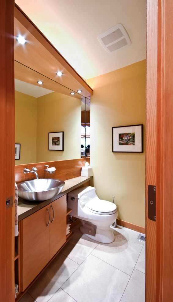 Пример оригинального дизайна: маленький туалет в современном стиле с плоскими фасадами, фасадами цвета дерева среднего тона, столешницей из бетона, унитазом-моноблоком, настольной раковиной, желтыми стенами, полом из известняка и серой плиткой для на участке и в саду