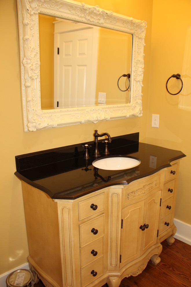シャーロットにある高級な小さなトラディショナルスタイルのおしゃれなトイレ・洗面所 (家具調キャビネット、白いキャビネット、黒いタイル、無垢フローリング、御影石の洗面台、黄色い壁、アンダーカウンター洗面器) の写真