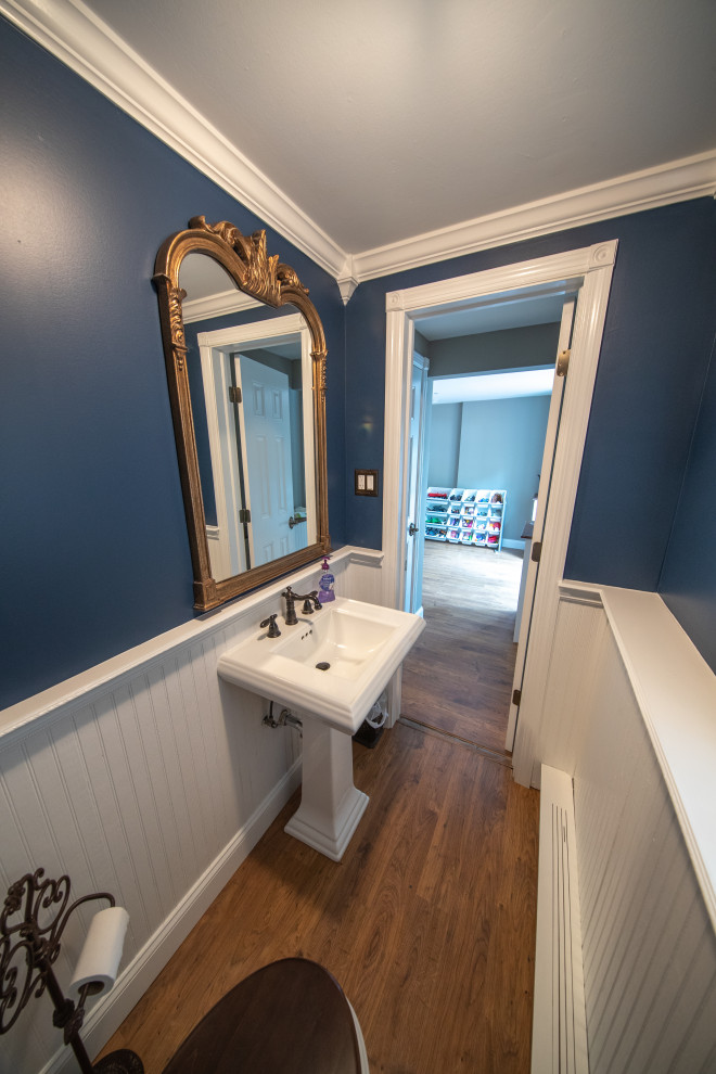 This is an example of a small classic cloakroom in New York with multi-coloured tiles, a two-piece toilet, laminate floors, a pedestal sink, brown floors and wainscoting.