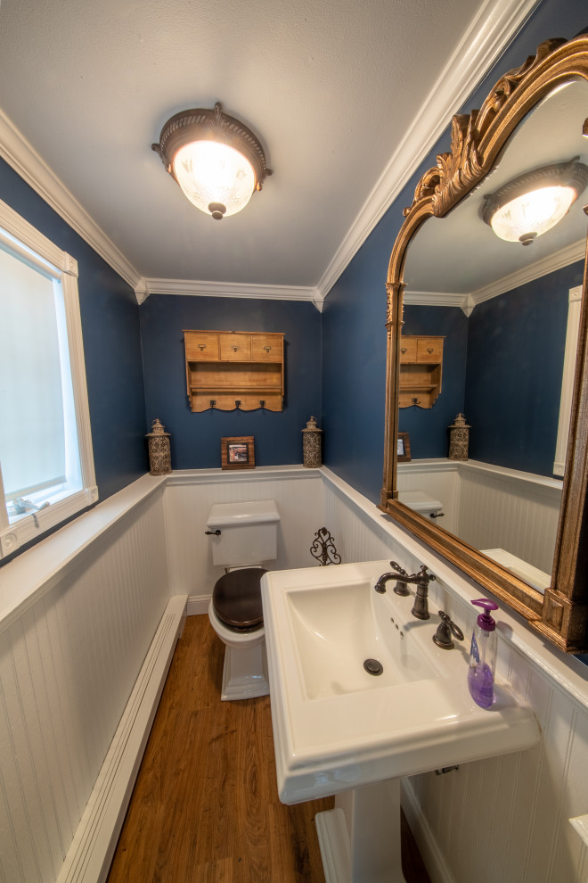 Imagen de aseo tradicional pequeño con sanitario de dos piezas, baldosas y/o azulejos azules, suelo laminado, lavabo con pedestal, suelo marrón y boiserie