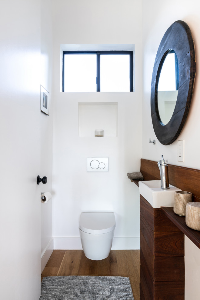 Kleine Moderne Gästetoilette mit braunen Schränken, Wandtoilette, weißer Wandfarbe, braunem Holzboden, braunem Boden und schwebendem Waschtisch in Los Angeles