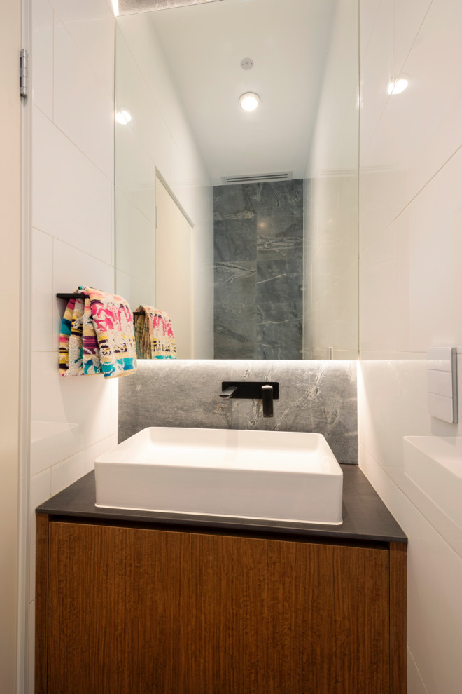 Foto di un piccolo bagno di servizio design con ante lisce, WC sospeso, piastrelle in pietra, pavimento in pietra calcarea, lavabo a consolle e mobile bagno sospeso