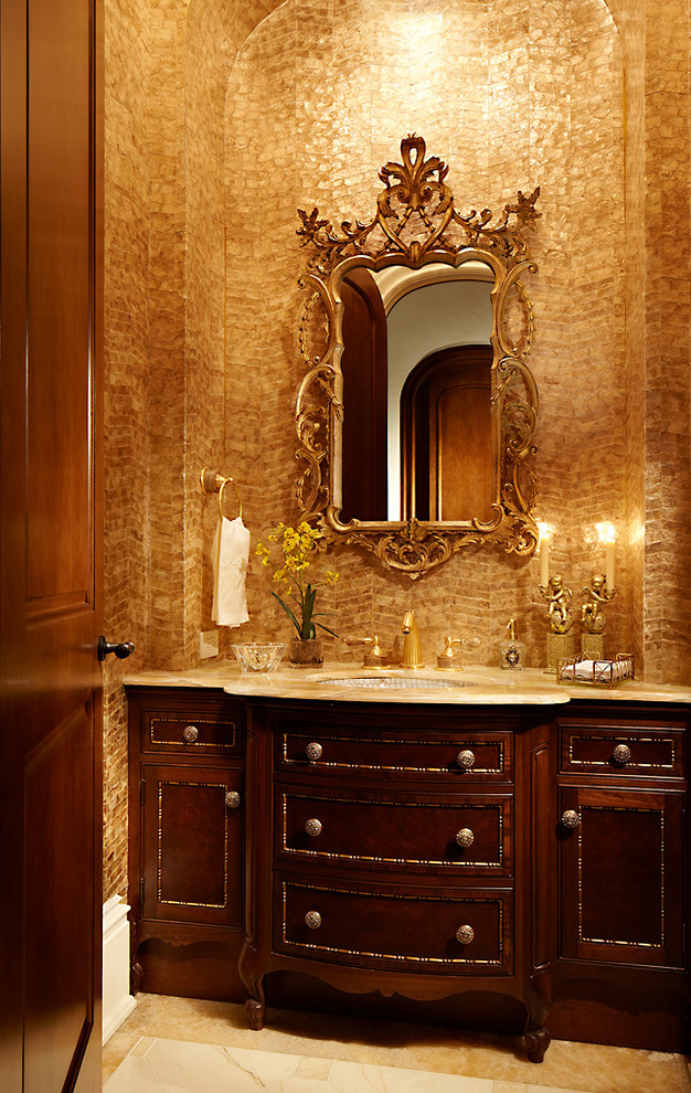 Inredning av ett klassiskt litet toalett, med ett undermonterad handfat, luckor med profilerade fronter, bänkskiva i onyx, beige kakel, stenkakel, marmorgolv och skåp i mörkt trä