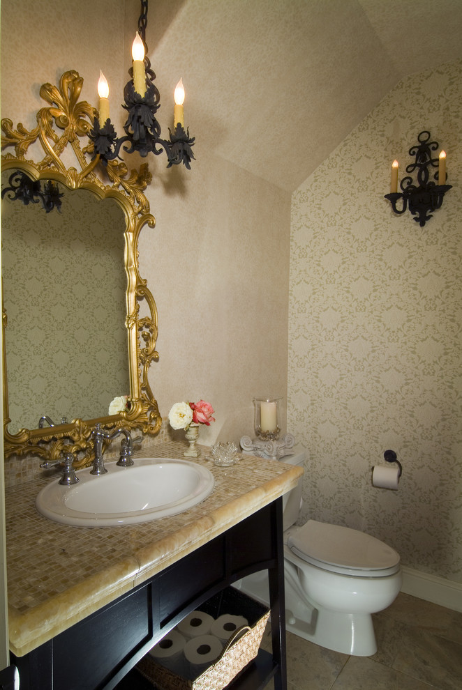 This is an example of a medium sized eclectic cloakroom in Other with freestanding cabinets, a two-piece toilet, beige walls, a built-in sink, beige floors, dark wood cabinets, travertine flooring, limestone worktops, beige worktops, a vaulted ceiling and wallpapered walls.