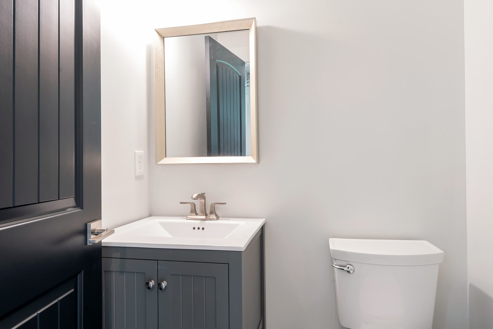 Foto på ett litet lantligt vit toalett, med möbel-liknande, blå skåp, en toalettstol med separat cisternkåpa, vita väggar, ett integrerad handfat och bänkskiva i akrylsten
