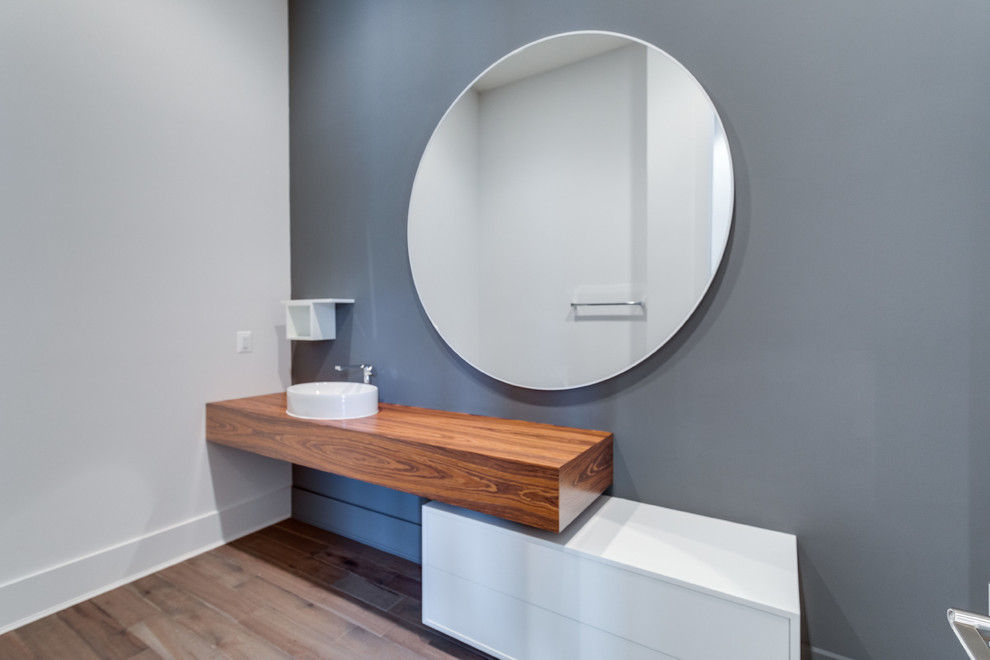 Exempel på ett klassiskt brun brunt toalett, med släta luckor, vita skåp, grå väggar, mörkt trägolv, ett fristående handfat, träbänkskiva och grått golv