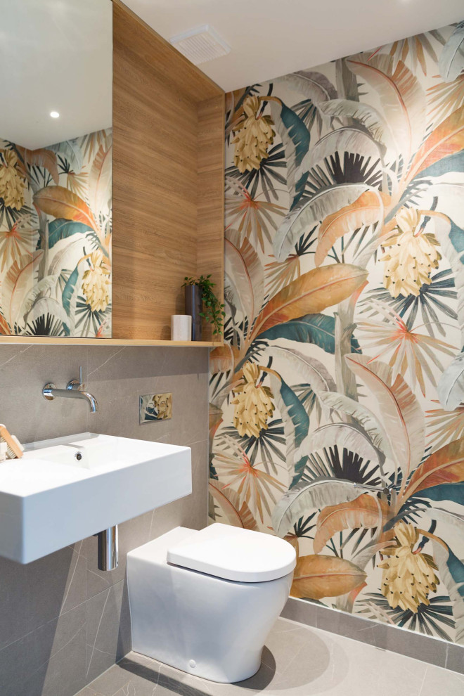 This is an example of a medium sized contemporary cloakroom in Sydney with a one-piece toilet, grey tiles, ceramic tiles, a wall-mounted sink and wallpapered walls.