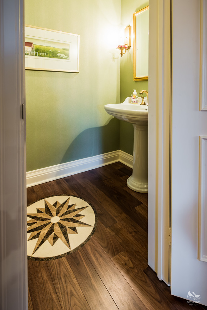Imagen de aseo tradicional pequeño con paredes verdes, suelo de madera en tonos medios y lavabo con pedestal
