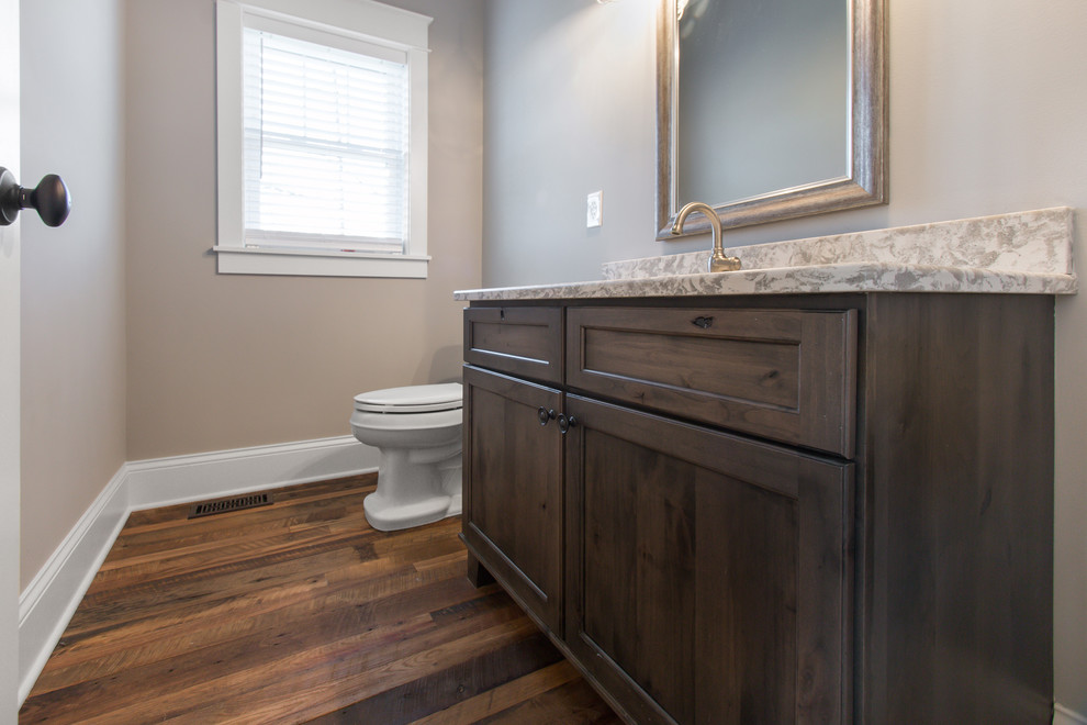 Foto på ett litet vintage toalett, med släta luckor, bruna skåp, en toalettstol med separat cisternkåpa, grå väggar, mellanmörkt trägolv, ett undermonterad handfat, bänkskiva i kvarts och brunt golv