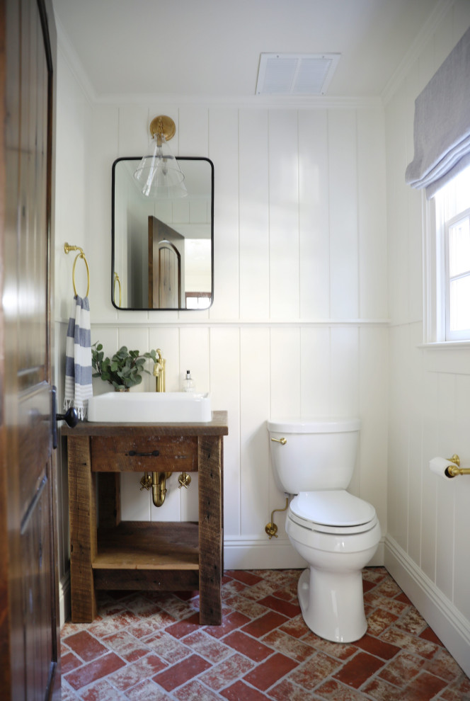 Small farmhouse cloakroom in New York with brown cabinets, white walls, brick flooring, a vessel sink, wooden worktops, red floors, brown worktops, a freestanding vanity unit and panelled walls.