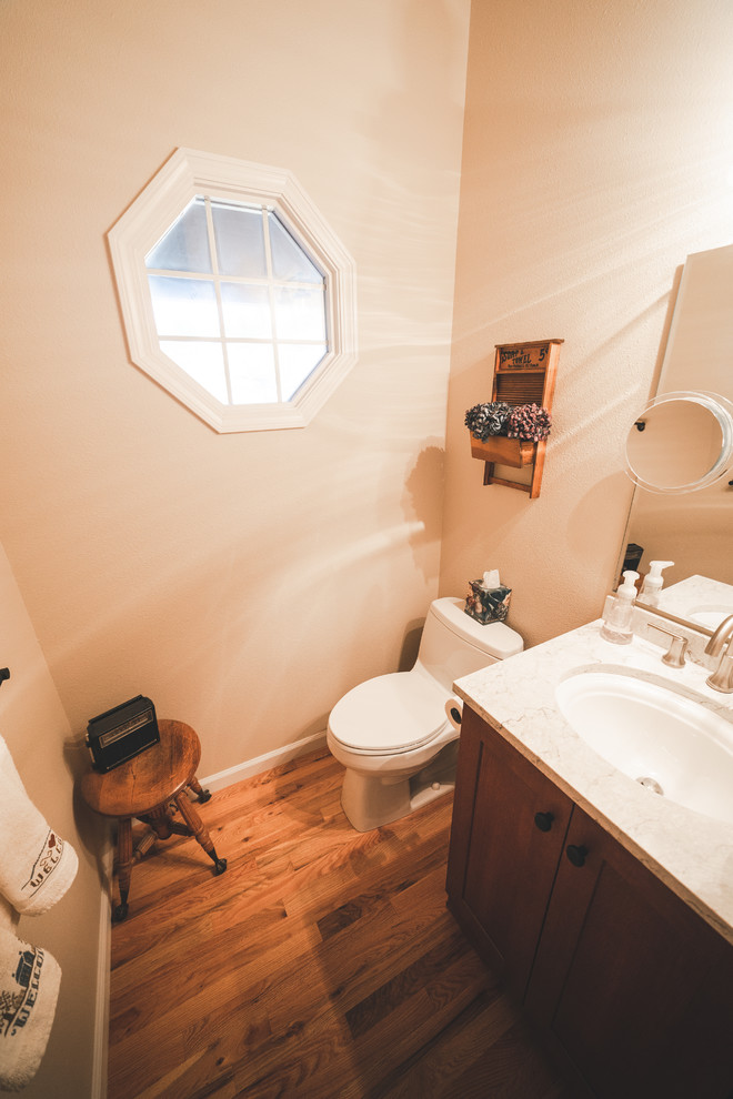 Lantlig inredning av ett mellanstort vit vitt toalett, med luckor med infälld panel, skåp i mellenmörkt trä, en toalettstol med hel cisternkåpa, beige väggar, mörkt trägolv, ett undermonterad handfat, bänkskiva i kvartsit och brunt golv