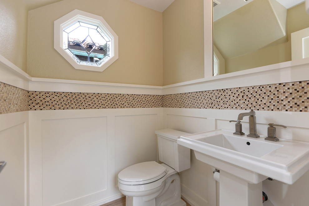 Small coastal cloakroom in San Diego with a pedestal sink, a one-piece toilet, brown tiles, beige walls, light hardwood flooring and mosaic tiles.