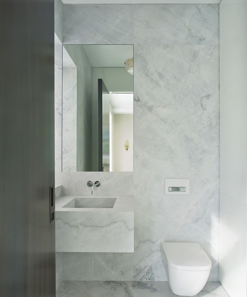 Inspiration for a modern gray tile and stone slab marble floor and gray floor powder room remodel in New York with glass-front cabinets, white cabinets, a wall-mount toilet, gray walls, a wall-mount sink and marble countertops