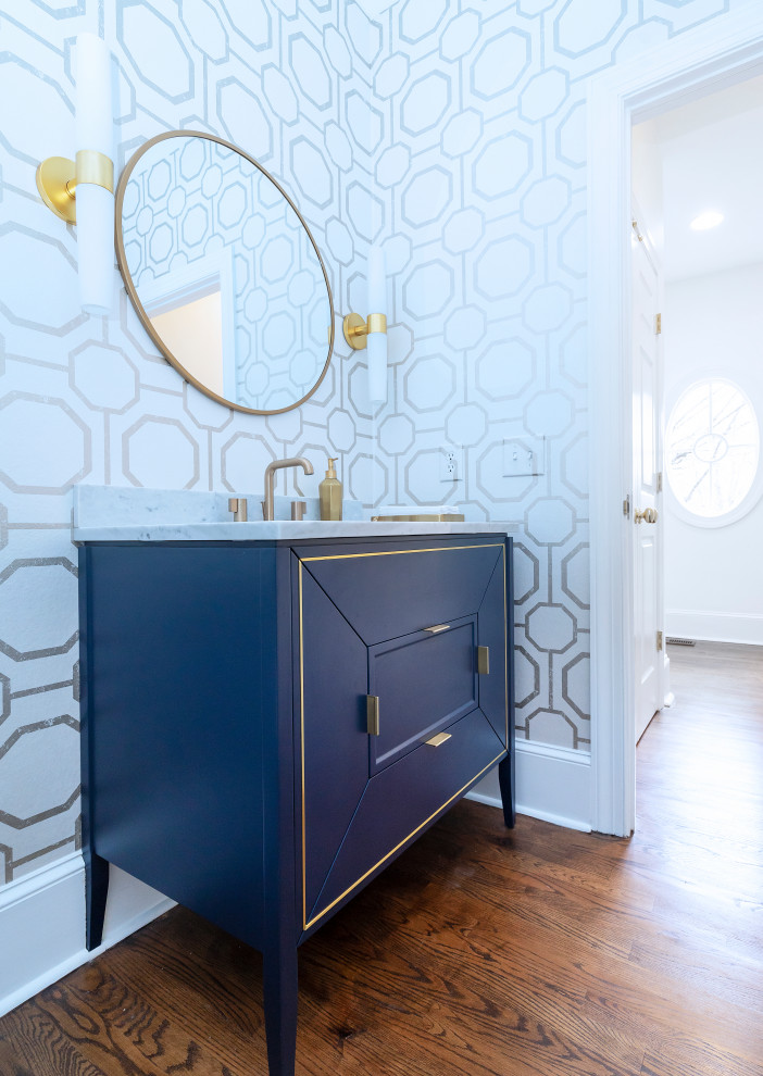 Example of a mid-sized transitional dark wood floor, brown floor and wallpaper powder room design in Philadelphia with raised-panel cabinets, blue cabinets, a console sink, marble countertops, white countertops and a freestanding vanity